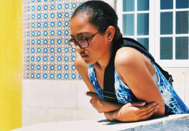 Young Cape Verdean woman observing passers-by in a typical Lisbon street whose facades are covered with tiles or azulejos.